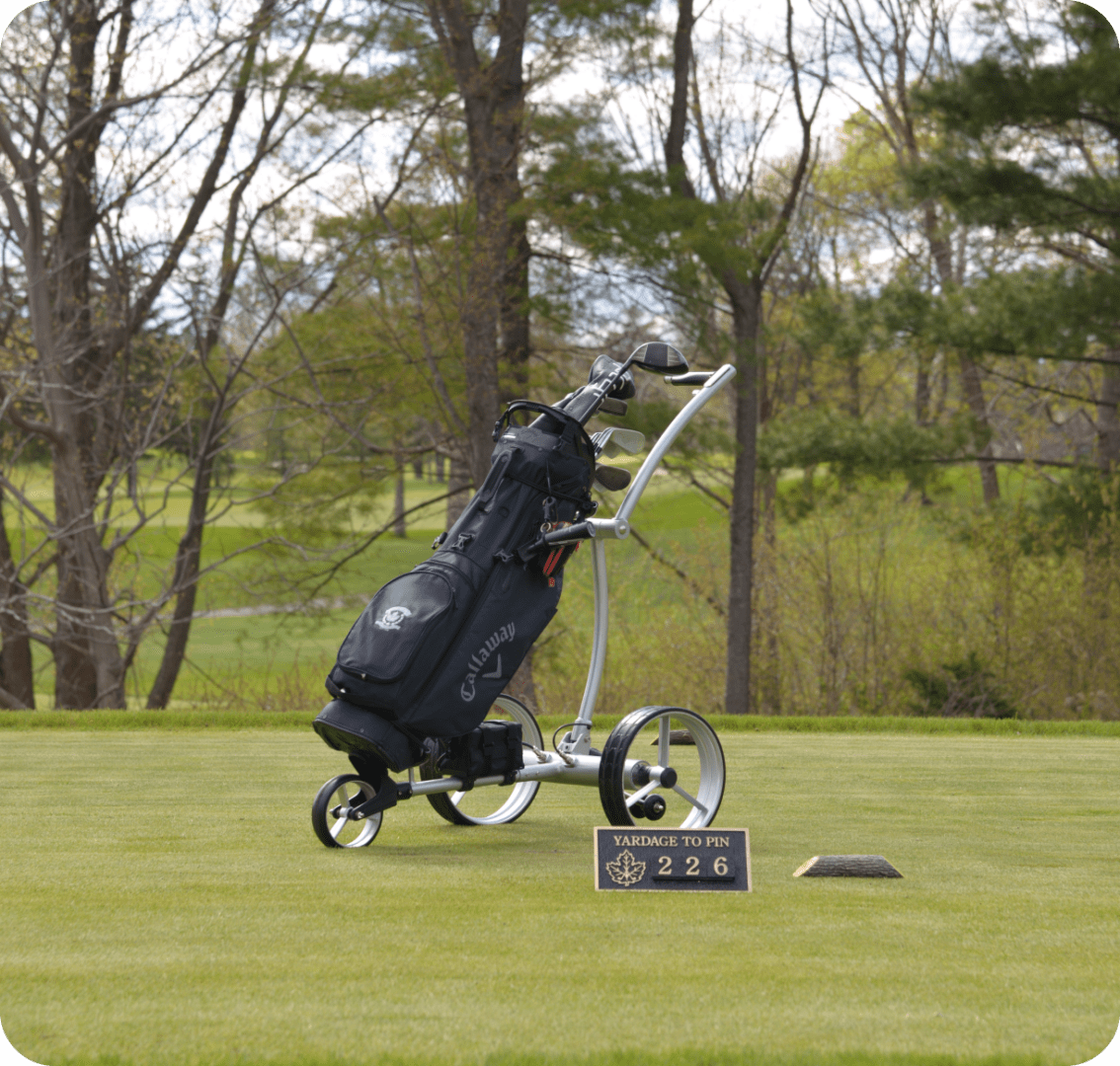 Golf bag on cart near distance marker.